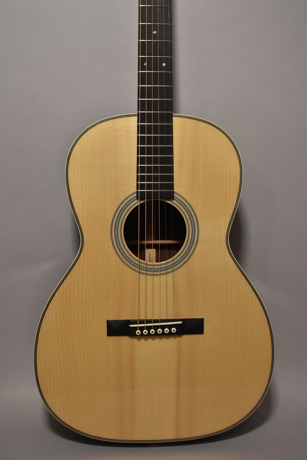 Full front view of a natural finish acoustic guitar, showing the light wood body, dark fretboard with diamond inlays, and black bridge.
