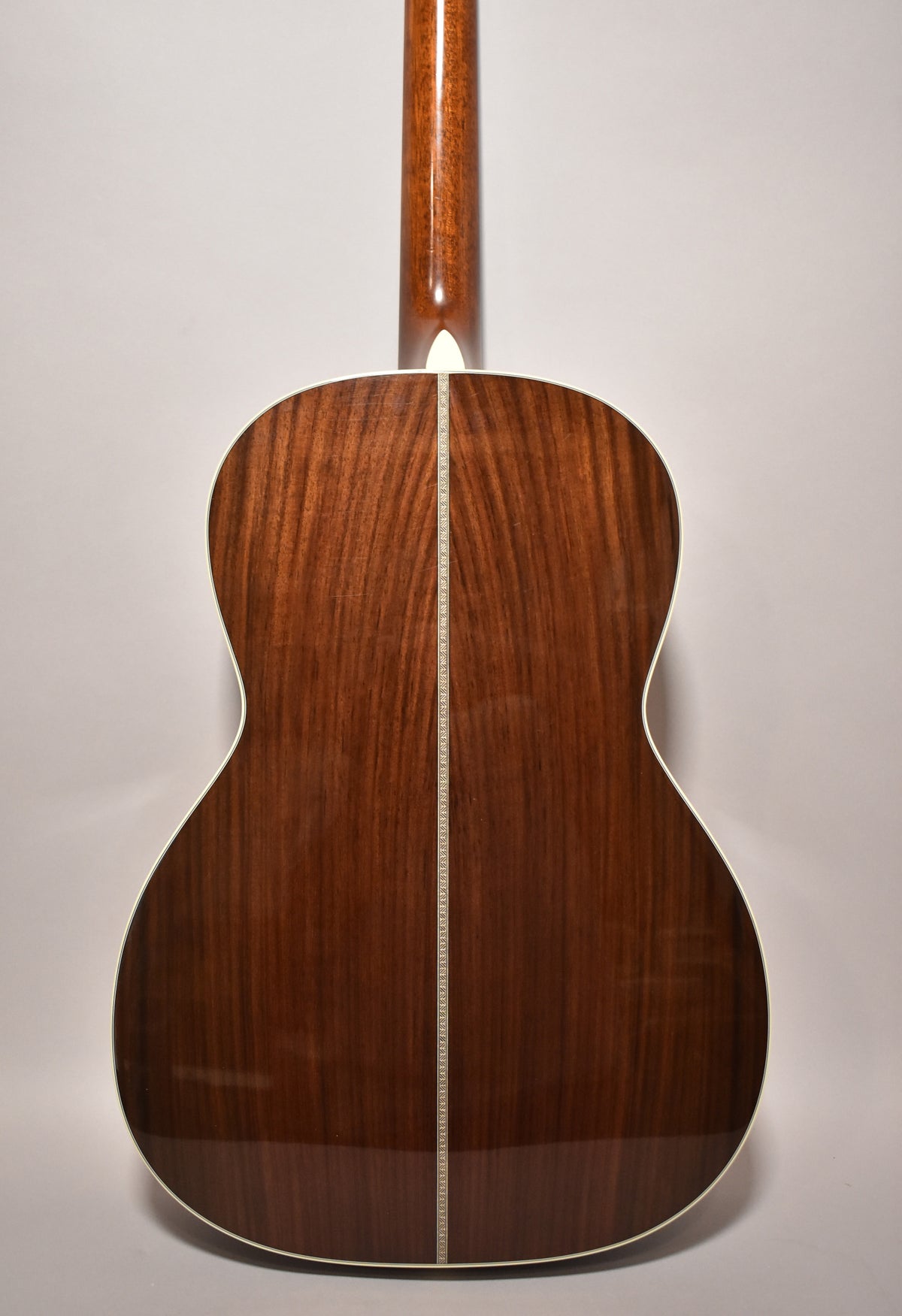 The back of the acoustic guitar, showing a dark brown wood grain with a glossy finish, white binding, and a decorative backstrip.