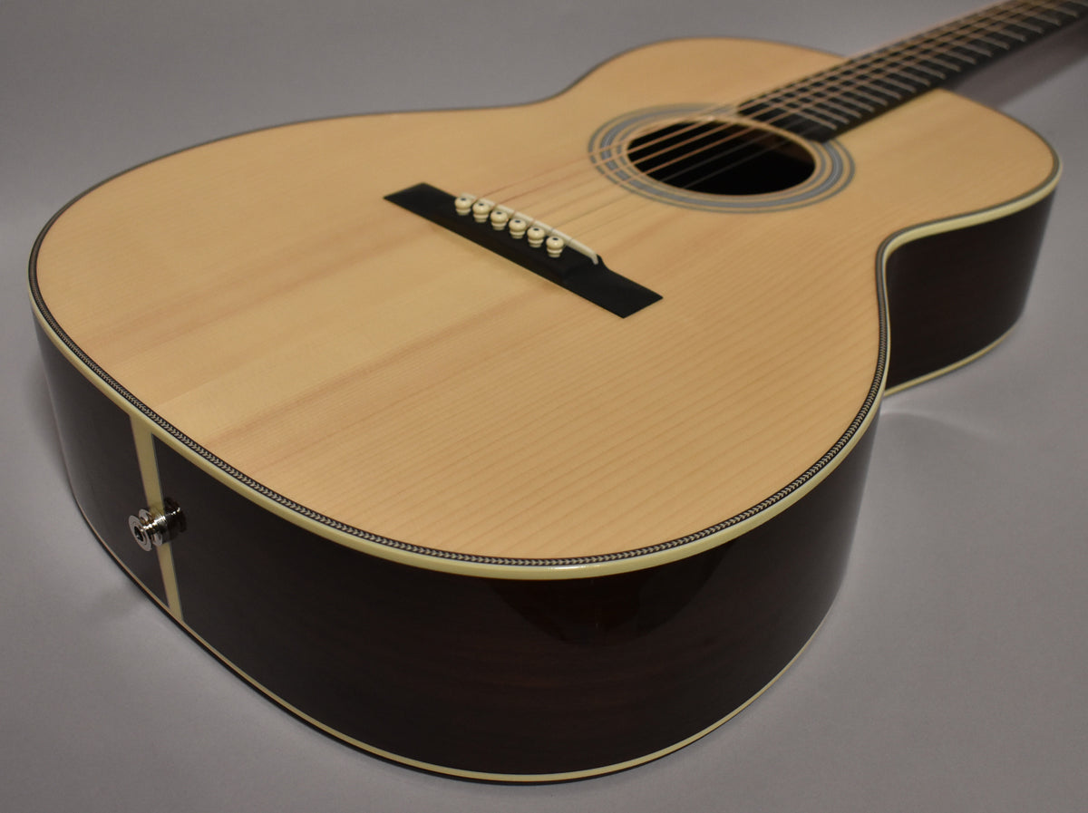 The acoustic guitar's natural finish top and dark sides are visible from the lower bout, with a chrome endpin jack and no visible wear.