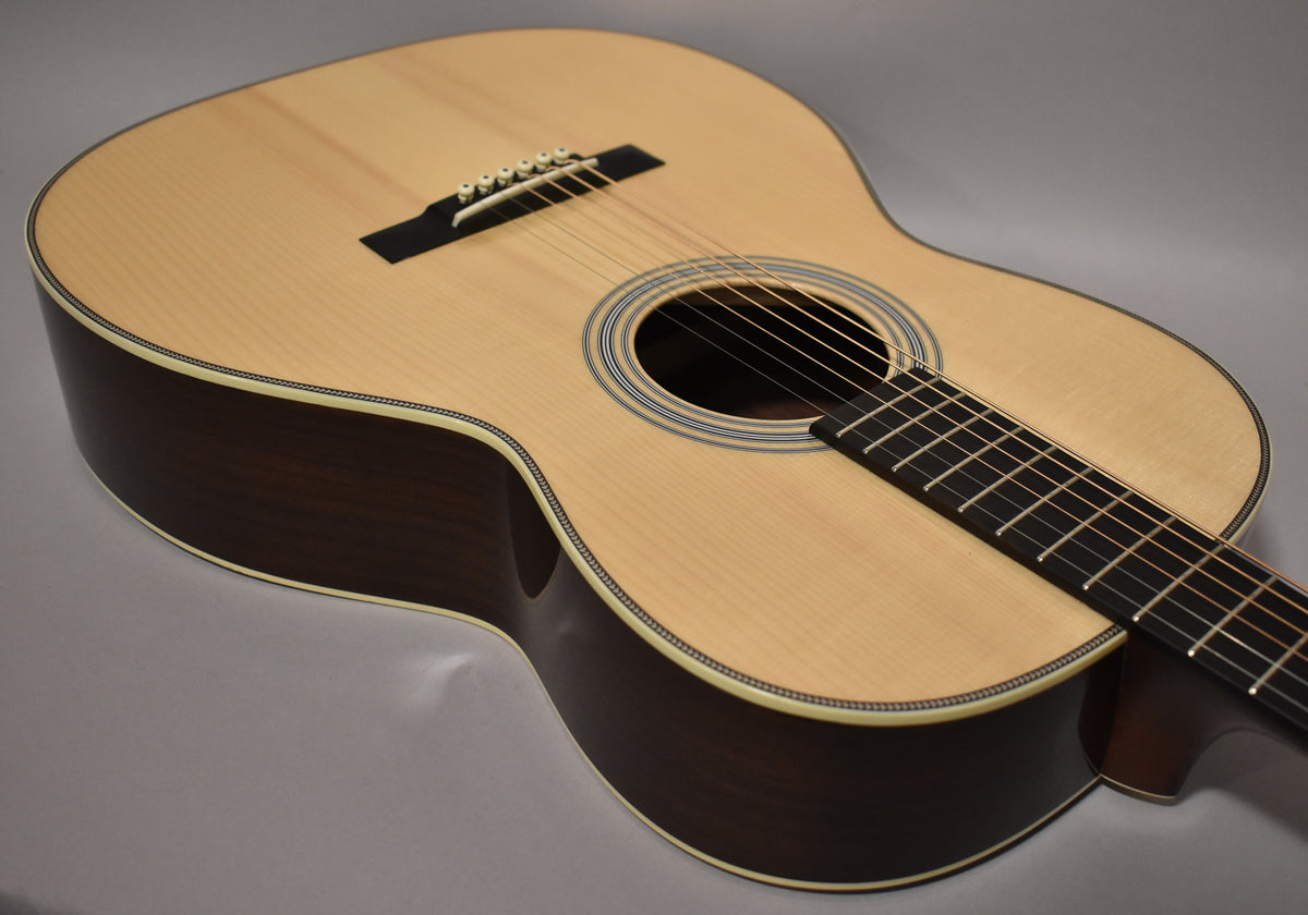 The acoustic guitar's natural finish top and dark sides are angled from the lower bout, showing the soundhole and bridge.