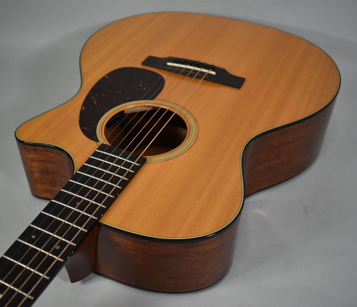 Overhead view of a light-wood acoustic guitar with a dark pickguard, showing the body, soundhole, bridge, and fretboard.