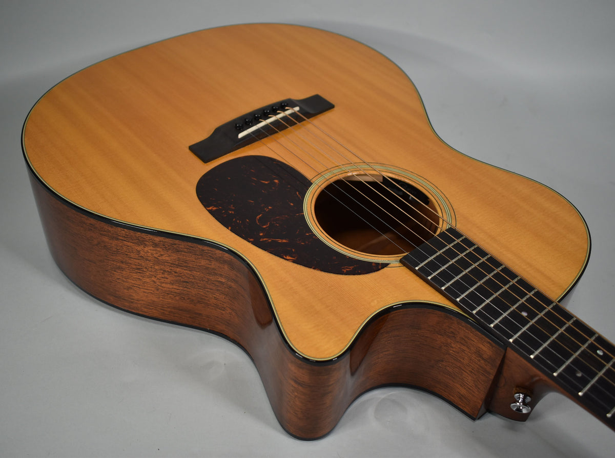 The acoustic guitar's light wood top and dark wood sides are visible from the upper bout to the cutaway, with a tortoiseshell pickguard.