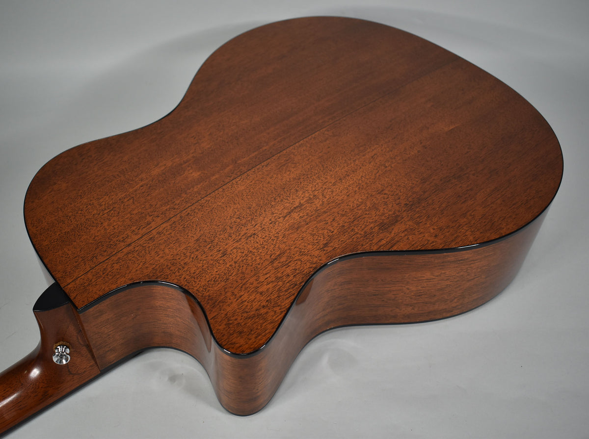 The back of a reddish-brown acoustic guitar, showing a cutaway body, a center seam, and a chrome strap button on the heel.
