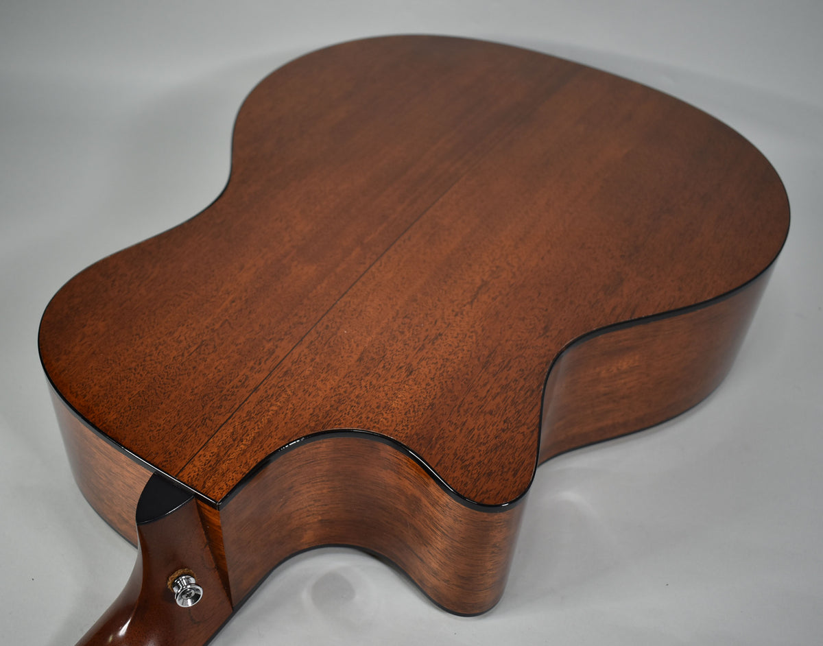 The guitar's dark brown back and sides are visible from the lower bout, with a single strap button on the neck heel.