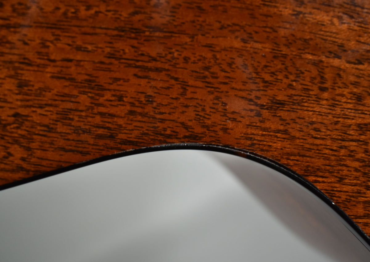 Close-up of the guitar's lower bout, showing the dark brown wood grain and the white pickguard with a thin black binding.
