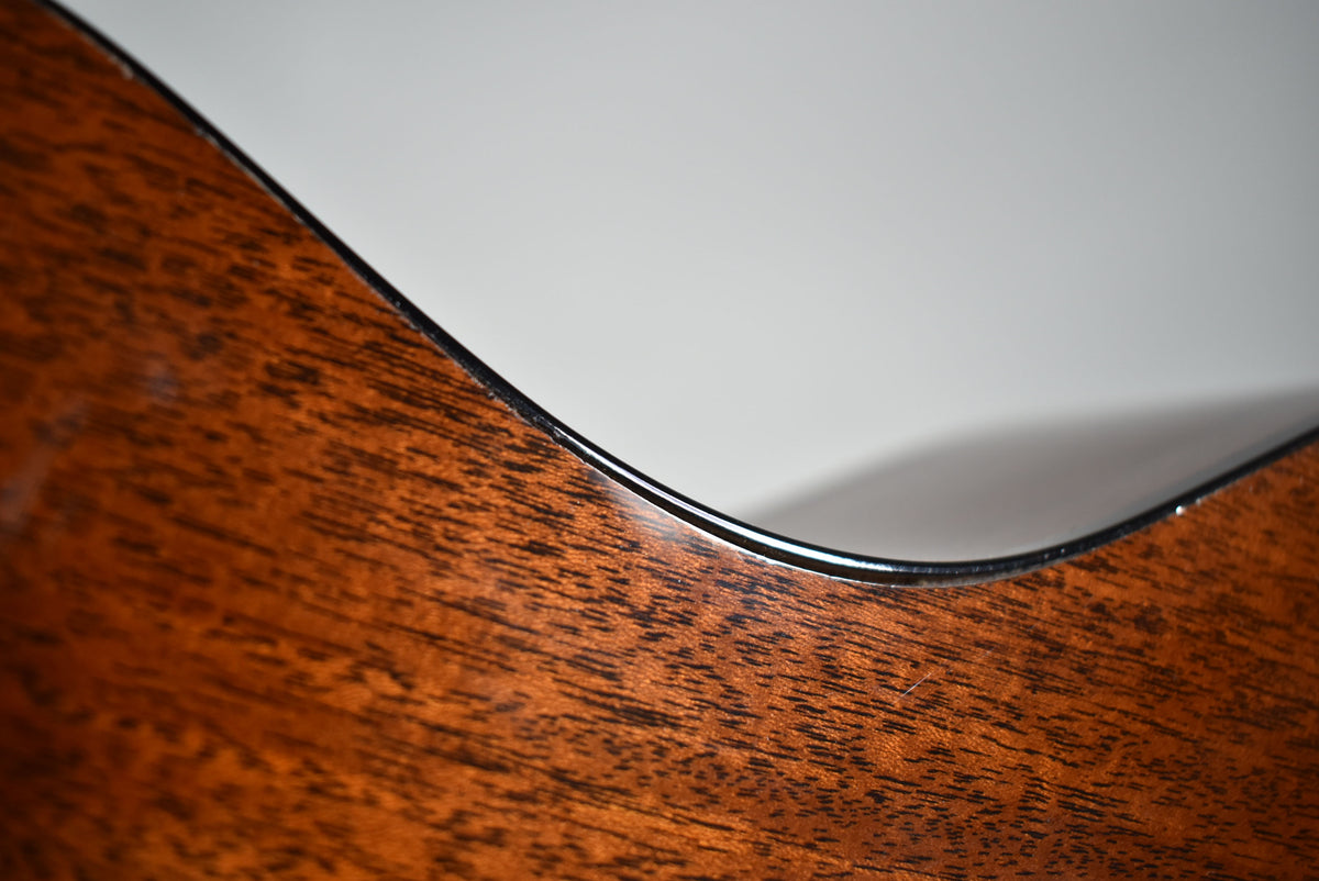 Close-up of the guitar's dark reddish-brown wood body with visible grain, showing the black binding along the curved edge.