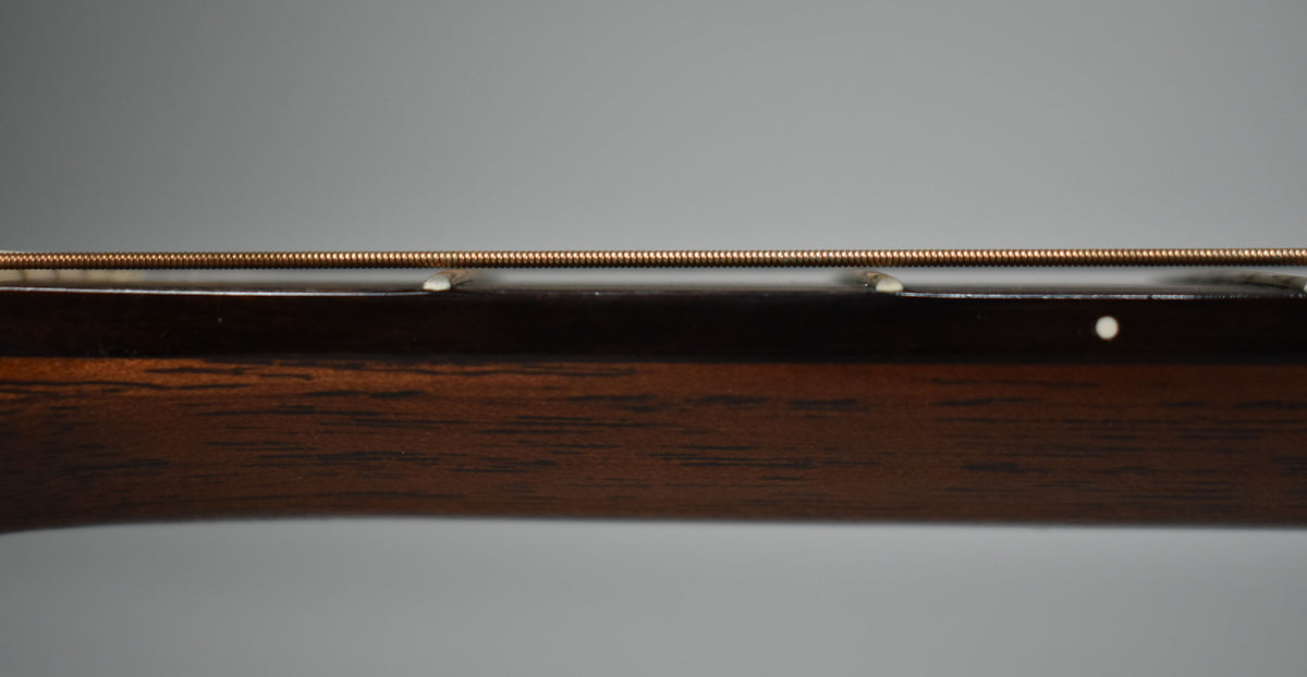 Close-up of the guitar's dark brown neck and fretboard from the side, showing a single bronze string and two white fret markers.