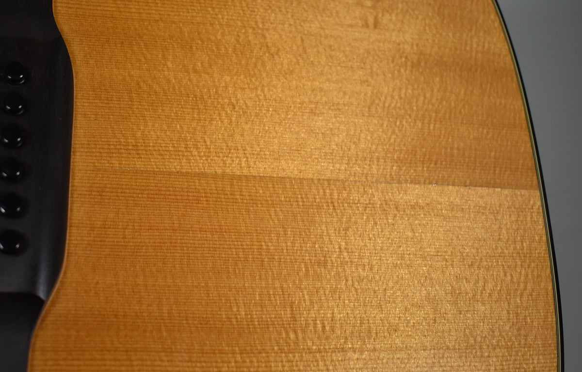 Close-up of the guitar's light brown spruce top, showing fine grain and a black control panel with five round knobs on the upper bout.