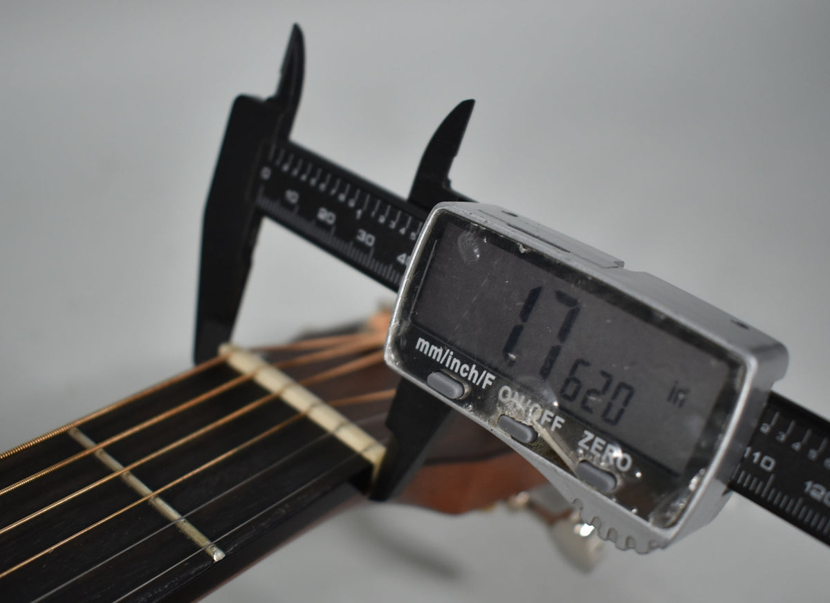 A digital caliper measures the guitar's nut width at 1.620 inches, with the dark fretboard and light nut visible.
