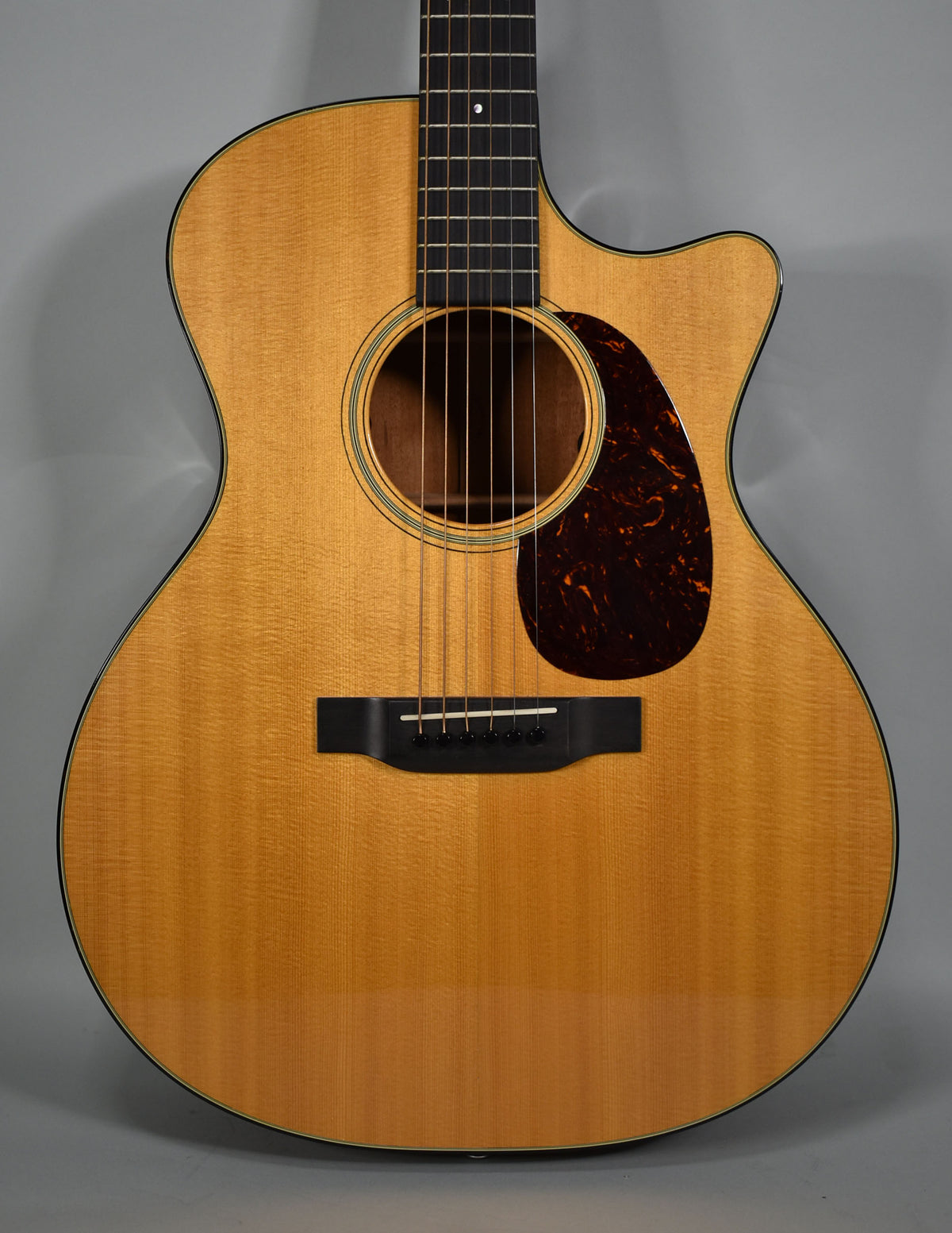 Full-frame view of a light-wood acoustic guitar with a dark tortoiseshell pickguard, black bridge, and cutaway body.