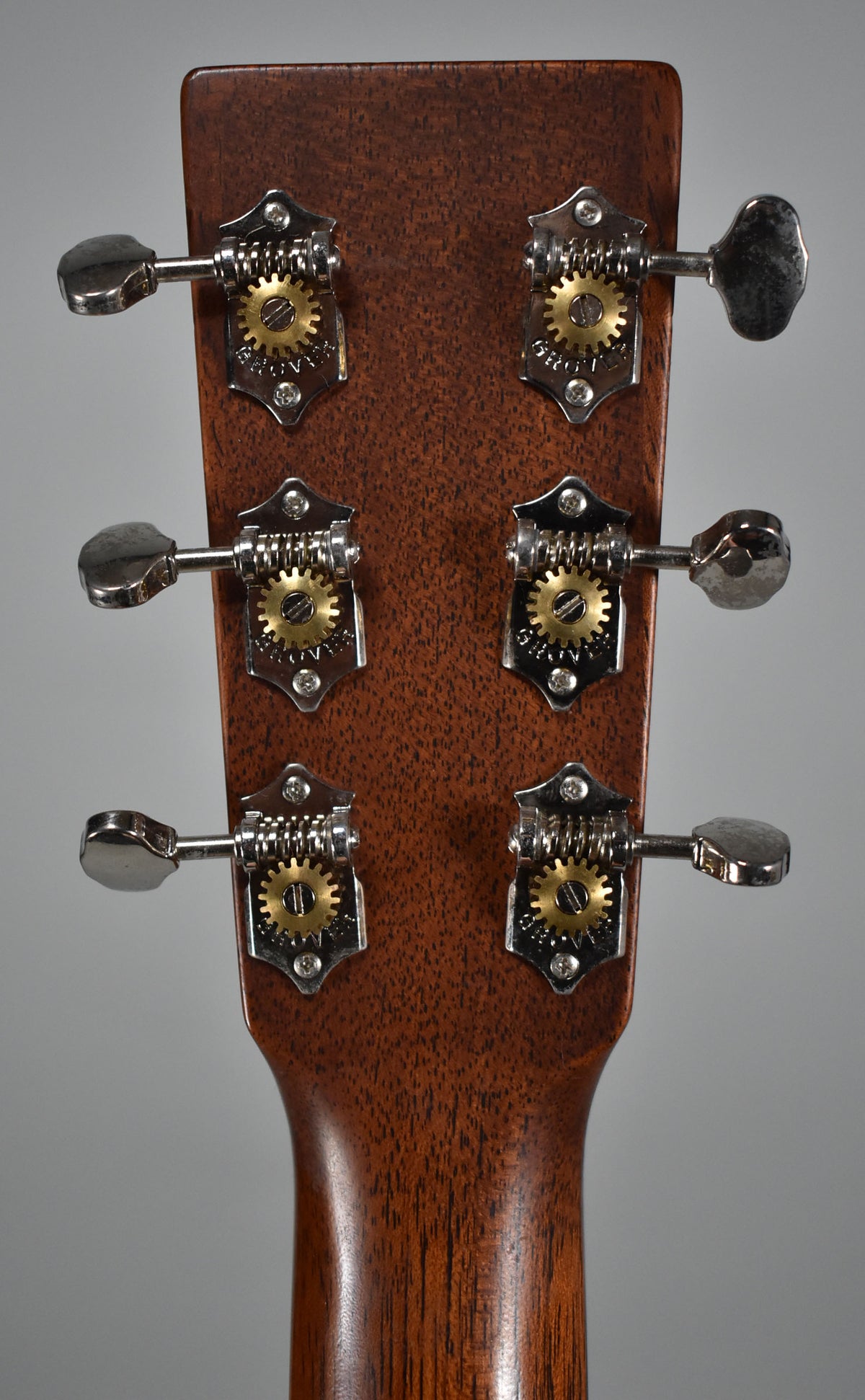 The back of the guitar's headstock and upper neck, showing six open-gear tuners with gold gears and chrome buttons on dark wood.