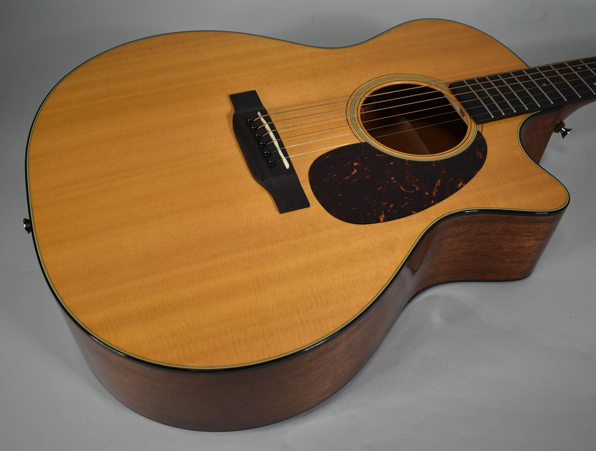 Overhead view of a light wood acoustic guitar with a dark tortoiseshell pickguard, black bridge, and cutaway body.
