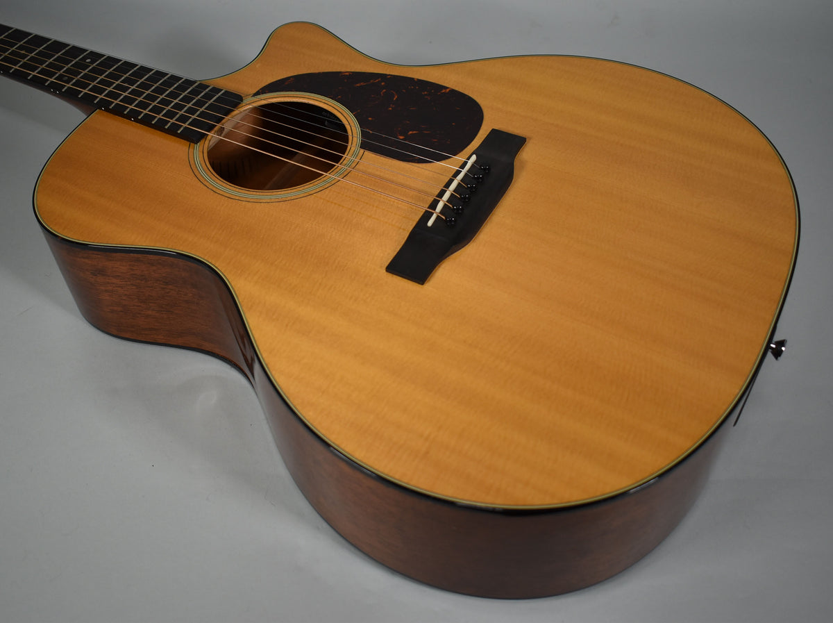 The acoustic guitar's light-colored top and dark sides are visible from the upper bout, with a black pickguard and bridge.