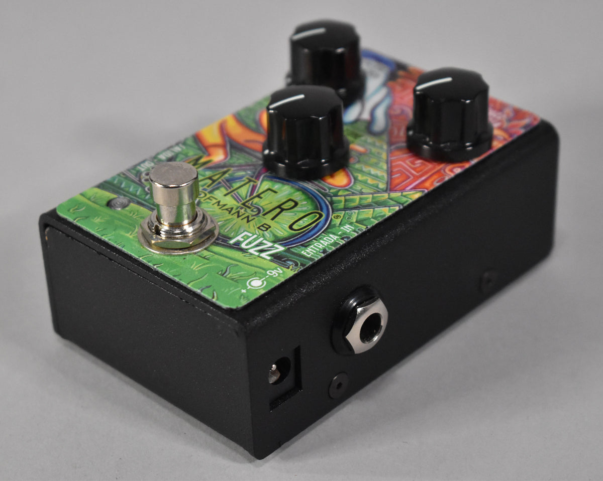 A black fuzz pedal with a colorful, abstract green and orange top panel, three black knobs, and a silver footswitch.