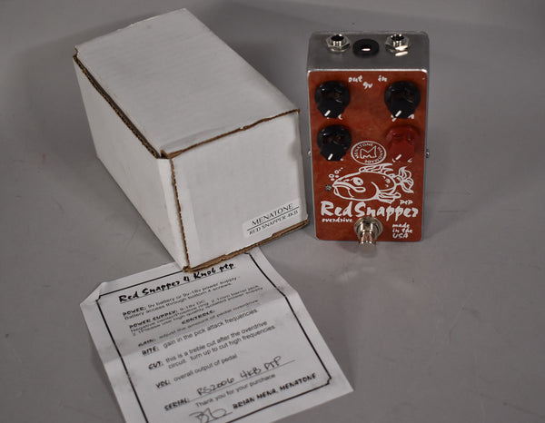 The red pedal with a fish graphic and four black knobs is angled beside its white box and instruction sheet.
