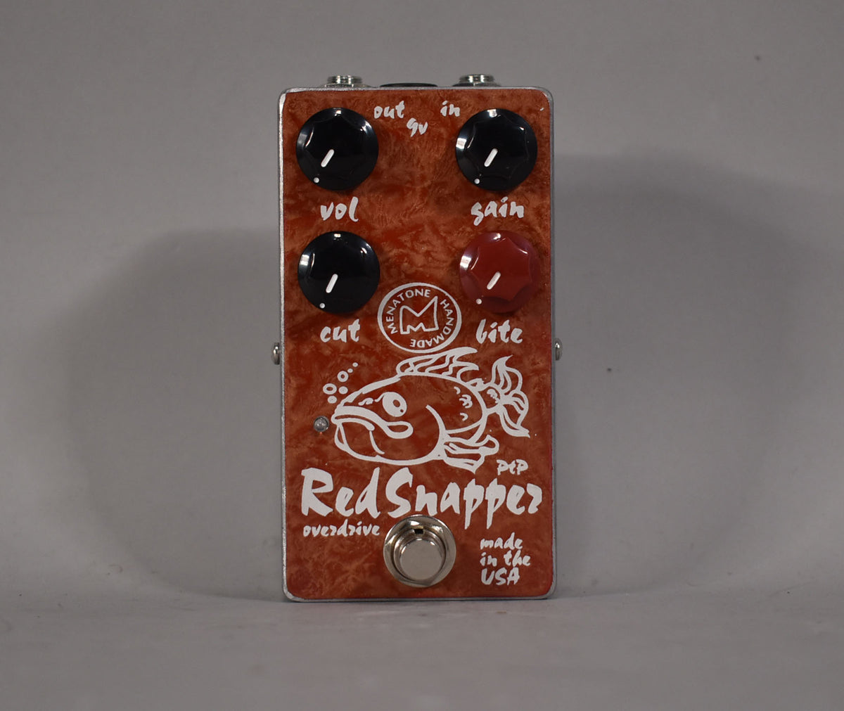 A top-down view of a rectangular red-orange pedal with a woodgrain finish, four knobs (three black, one red), and a silver footswitch.