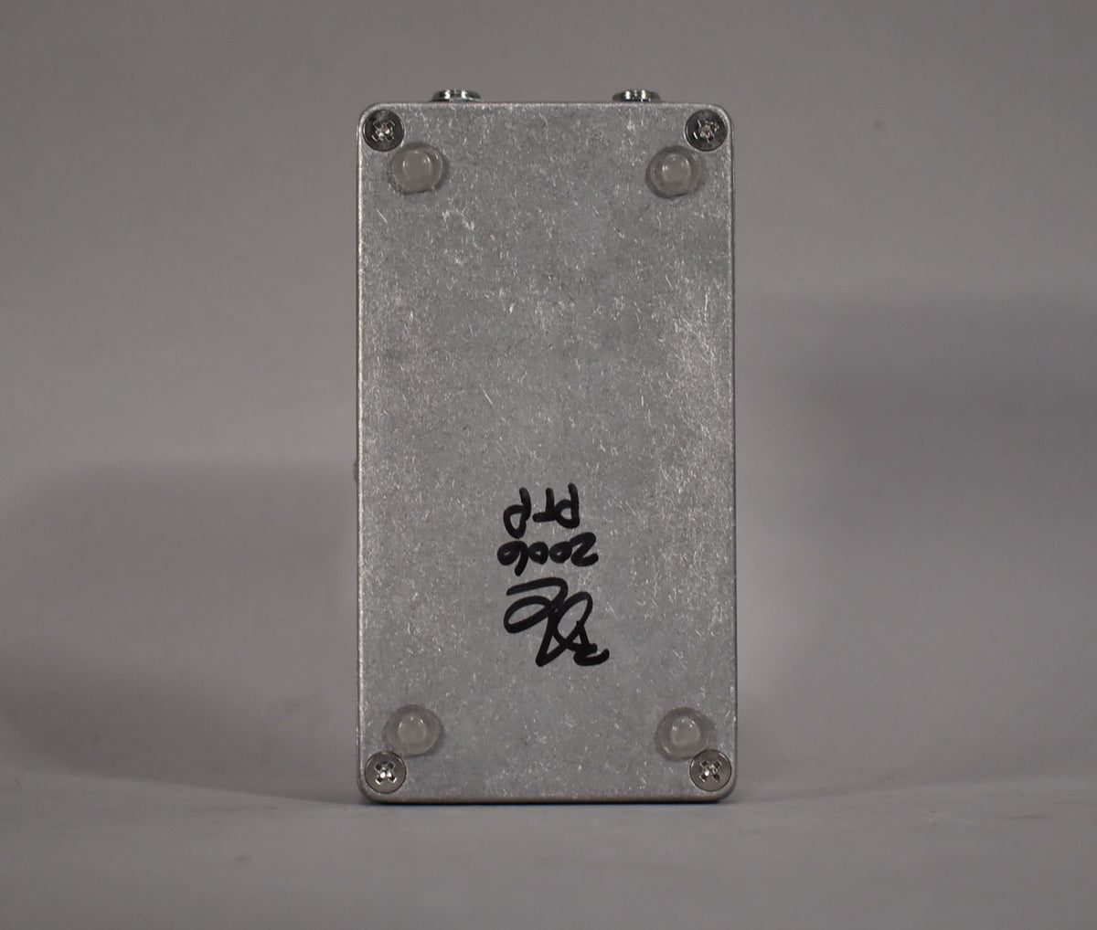 The pedal's brushed silver bottom plate is visible, with four clear rubber feet and black handwritten text "2006 PTP" and a signature.