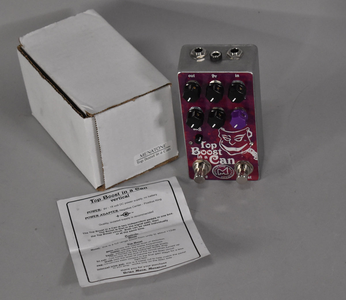 The pedal, box, and manual are angled from above, showing the pedal's purple face with six black knobs and two footswitches.