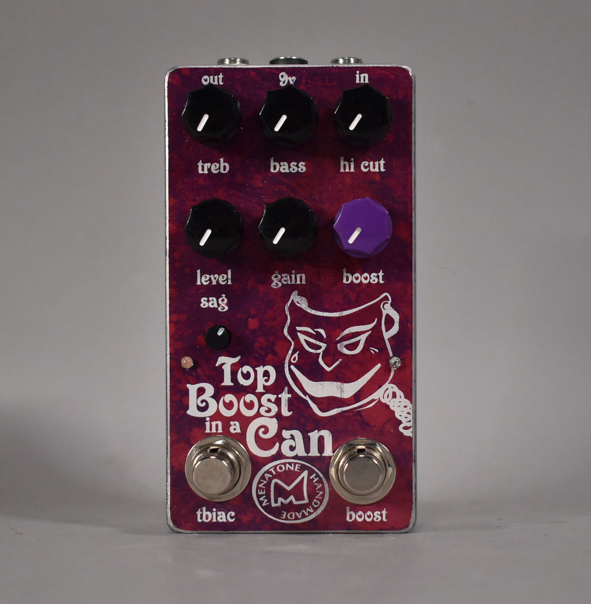 A top-down view of a purple pedal with a white cartoon face, six black knobs, one purple knob, and two footswitches.