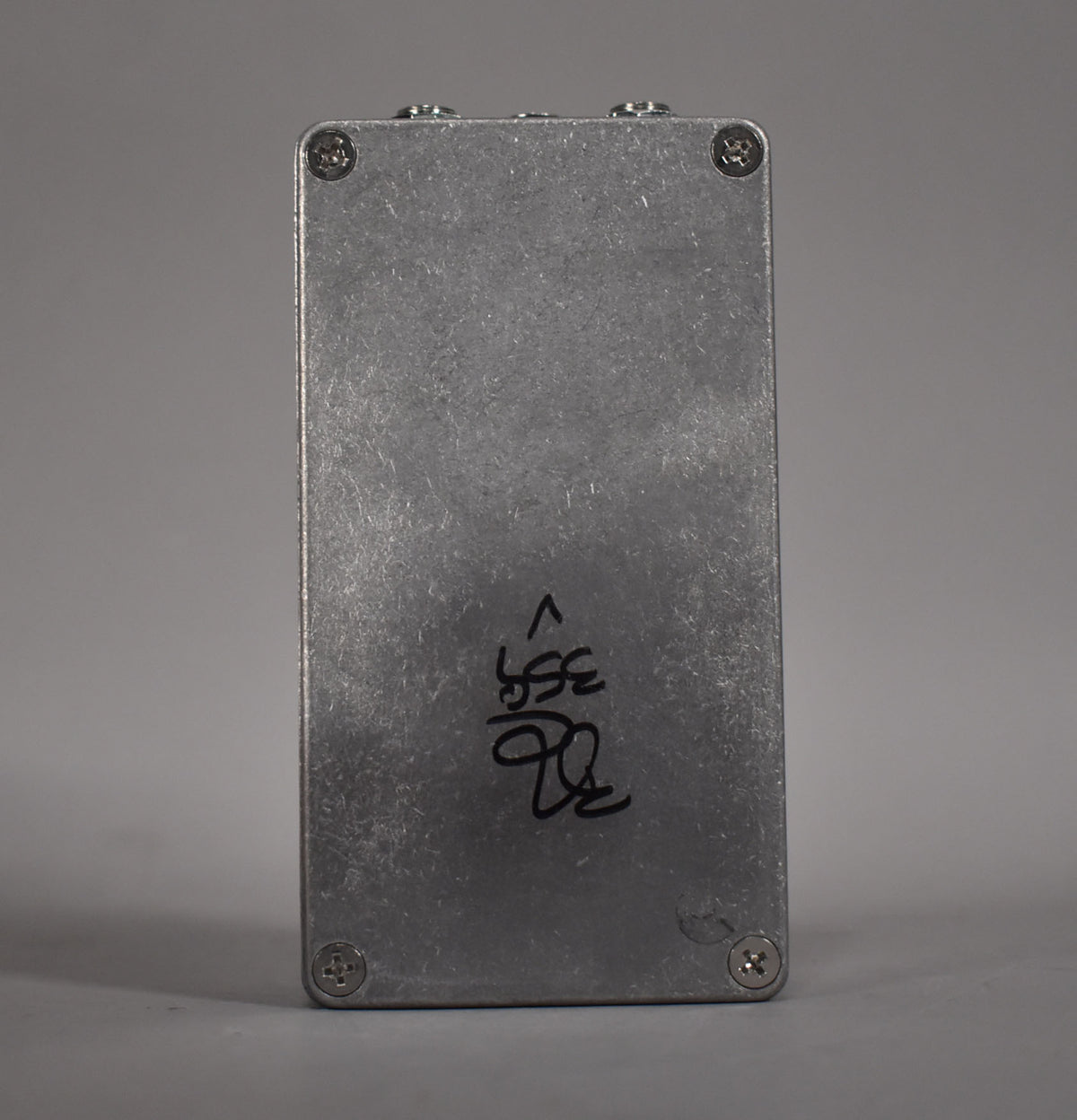 The pedal's brushed aluminum bottom plate is visible, secured by four Phillips head screws, with black handwritten markings.