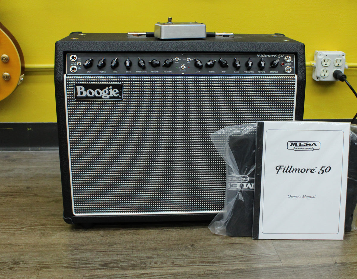 Front view of a black combo amp with a silver grille, black control knobs, and an owner's manual and footswitch beside it.