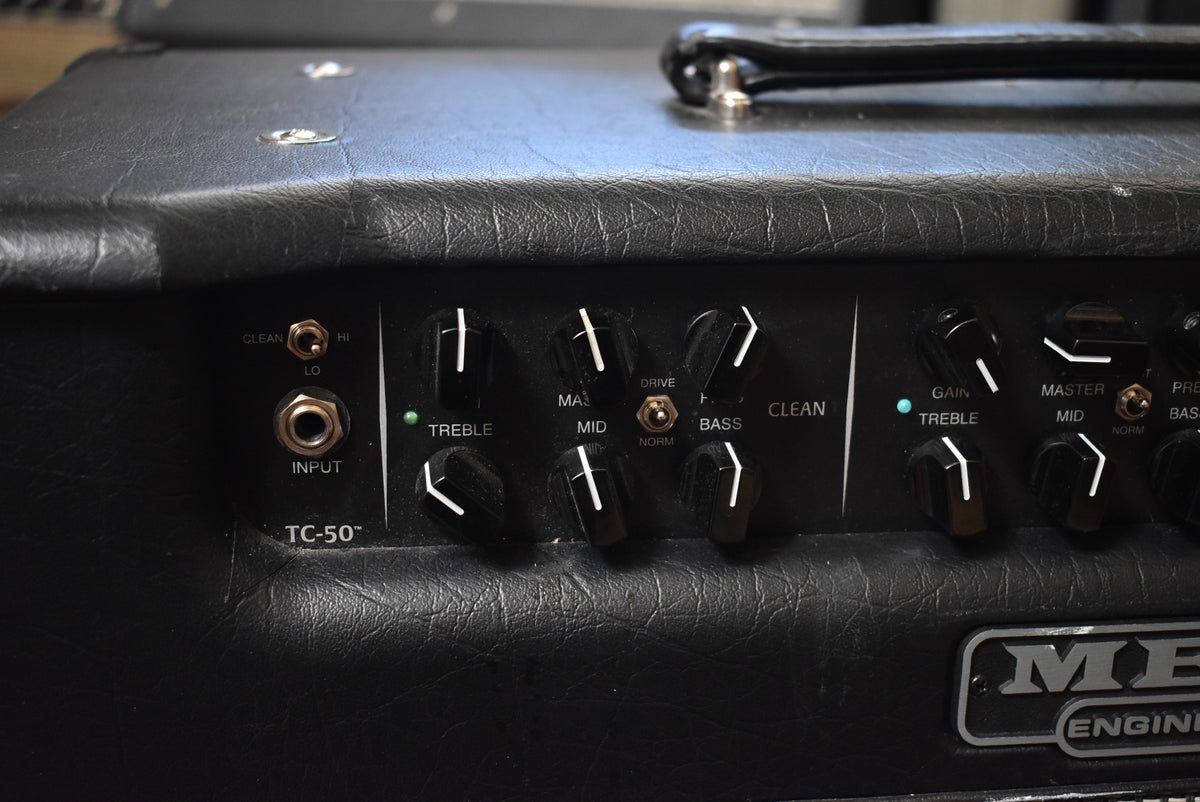 Close-up of the black amp's control panel, showing input jacks, tone knobs, and a green indicator light, with minor scuffs on the tolex.