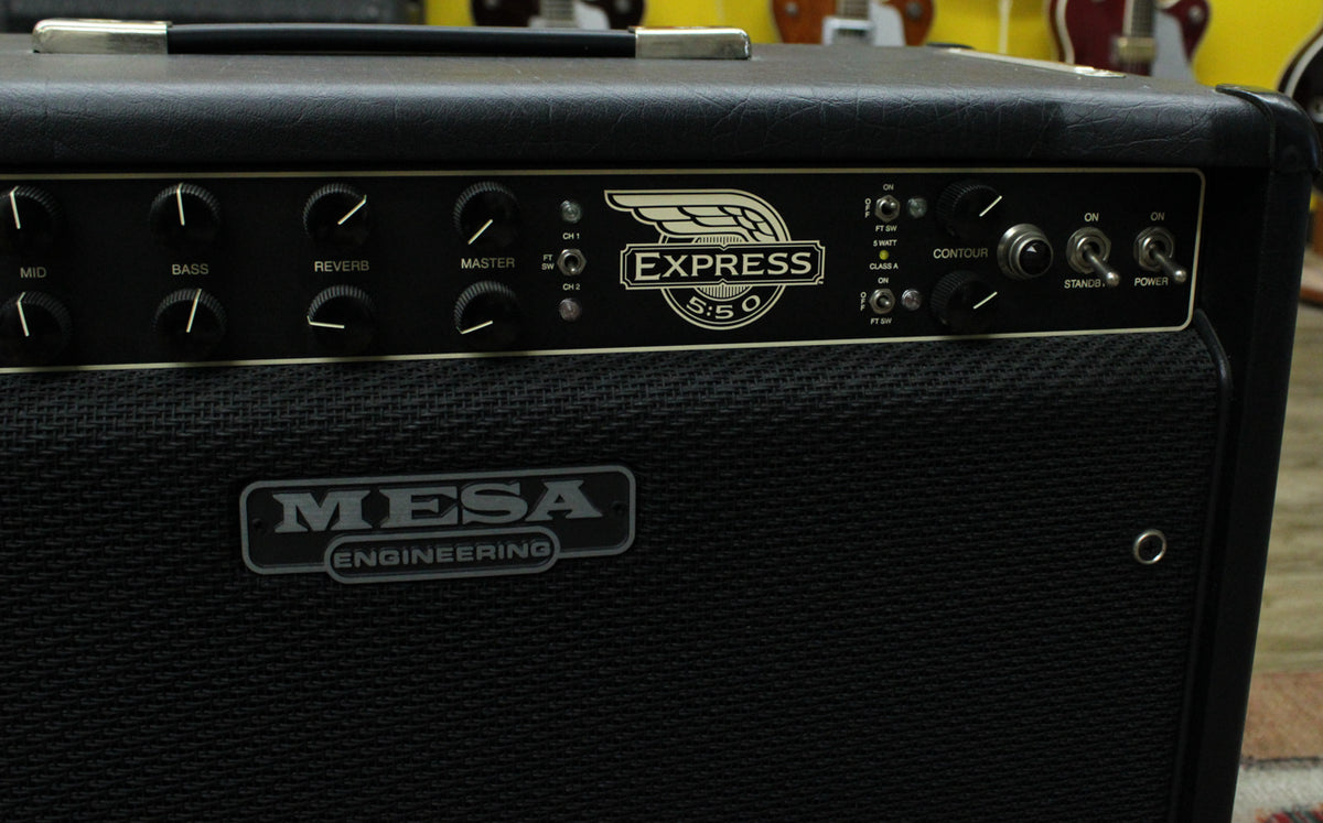 Close-up of the black tolex amp's control panel and speaker grille, showing numerous black knobs and three chrome toggle switches.