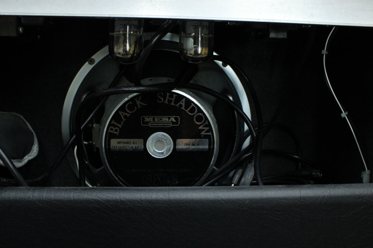 Rear view of the amp's interior, showing two glowing vacuum tubes above a black speaker with a silver dust cap and white surround.