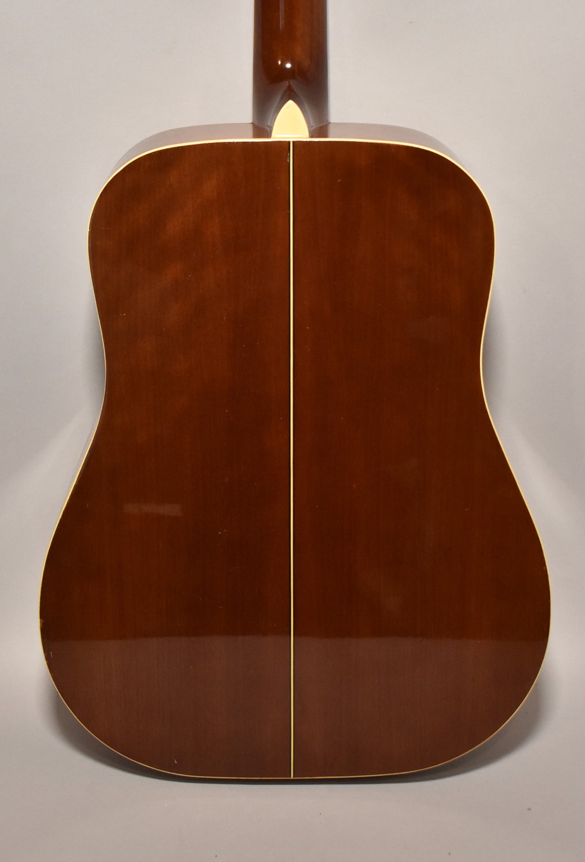 The guitar's back is a rich brown with a glossy finish, featuring a light-colored center strip and binding, with minor surface wear.