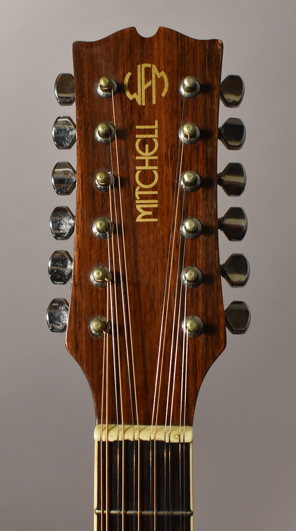 Close-up of the dark brown headstock, showing 12 tarnished chrome tuners, a cream nut, and light wear on the top edge.