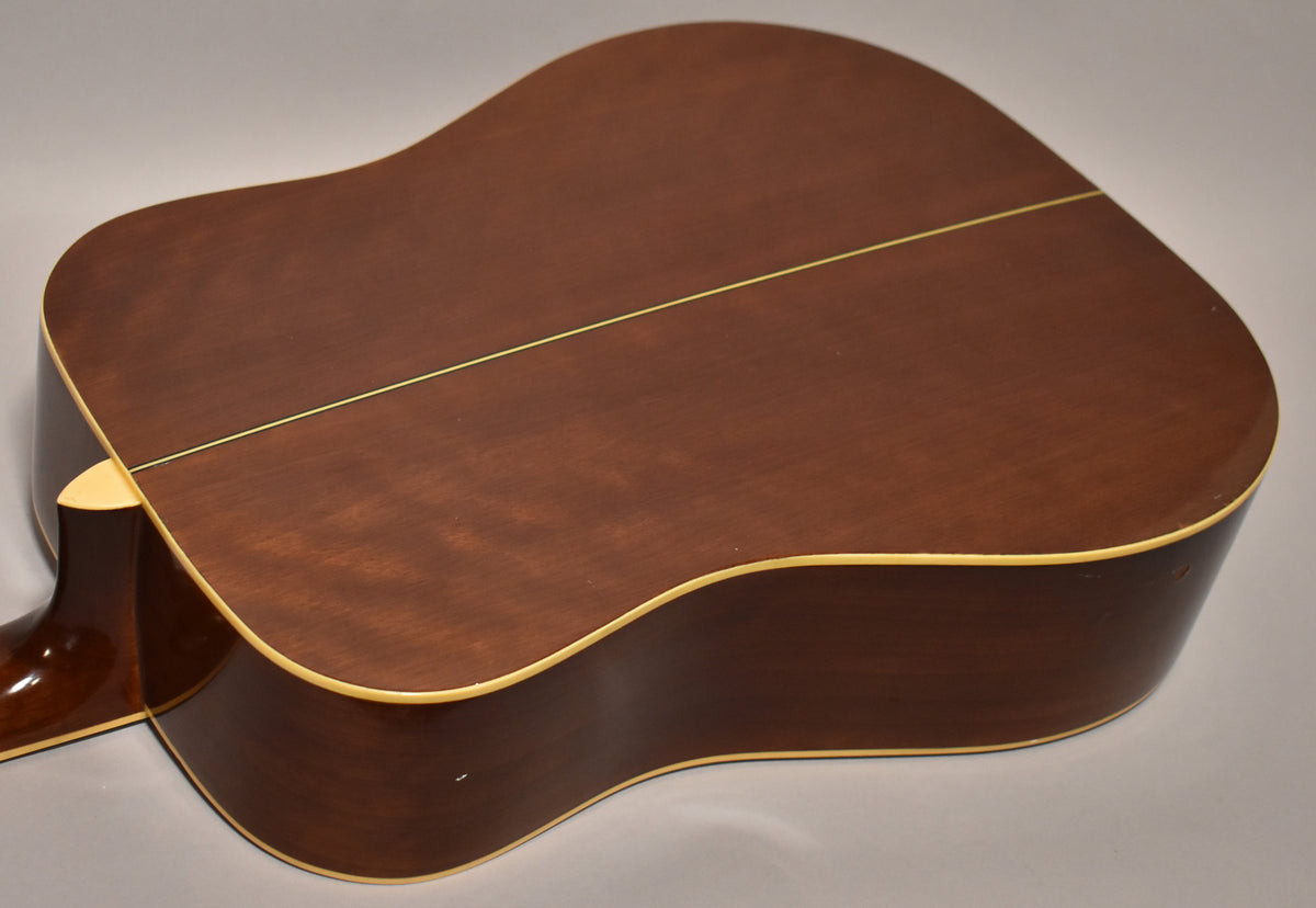 The back of a dreadnought acoustic guitar, showing its dark brown finish, cream binding, and a light center strip.