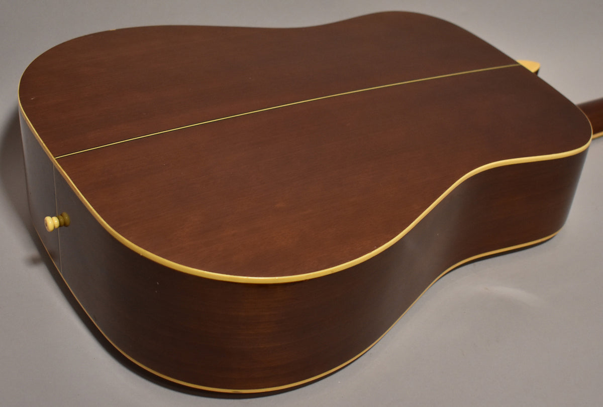 The back and side of the dreadnought are dark brown with a matte finish and cream binding, showing light wear and a strap button.