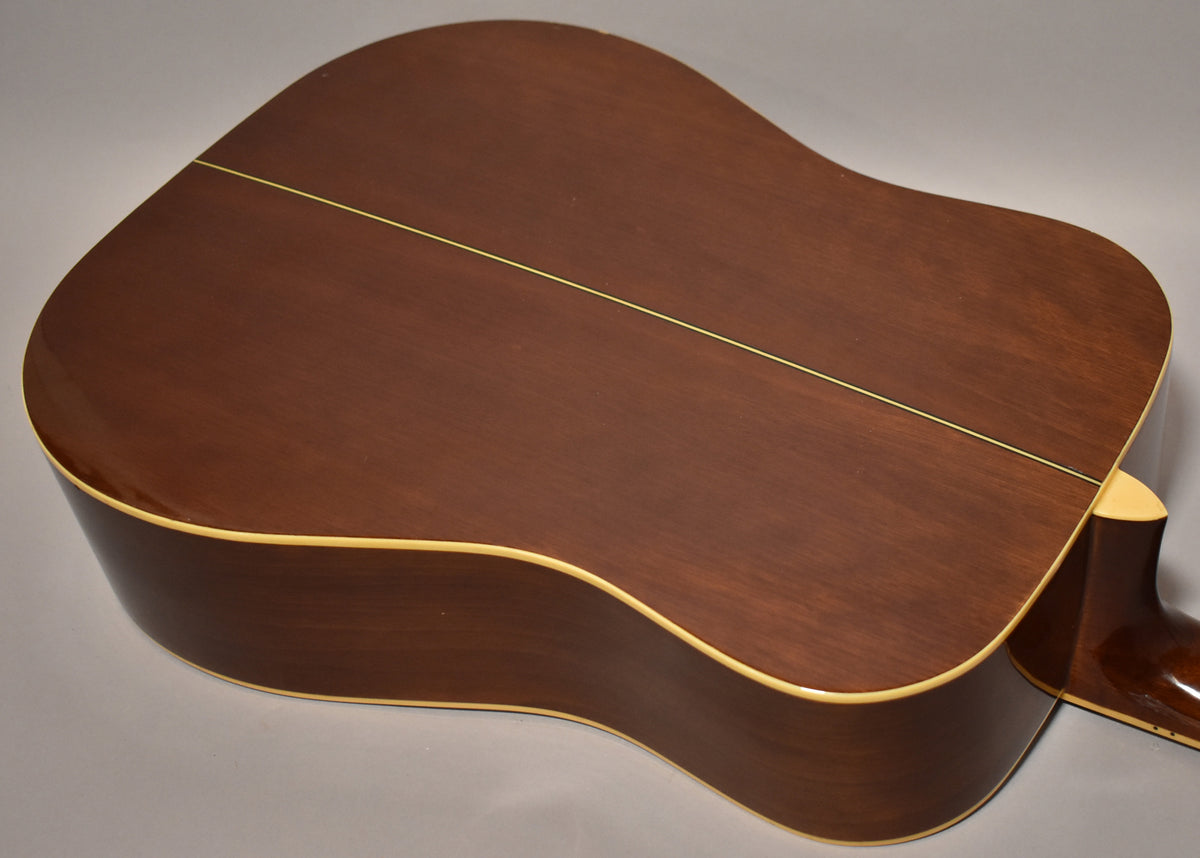 The back of a natural finish dreadnought acoustic guitar, showing the dark brown wood grain, a light center strip, and cream binding.