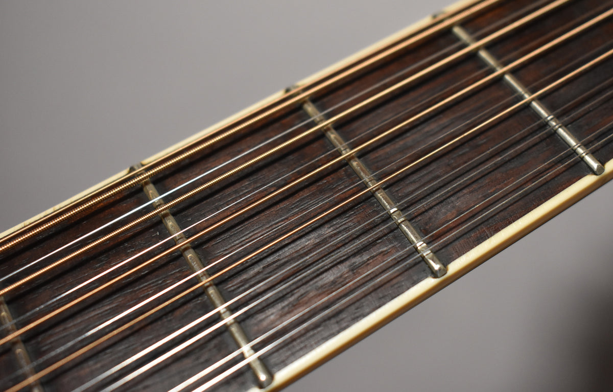 Close-up of the dark rosewood fretboard with 12 strings, showing light wear and some fret pitting.