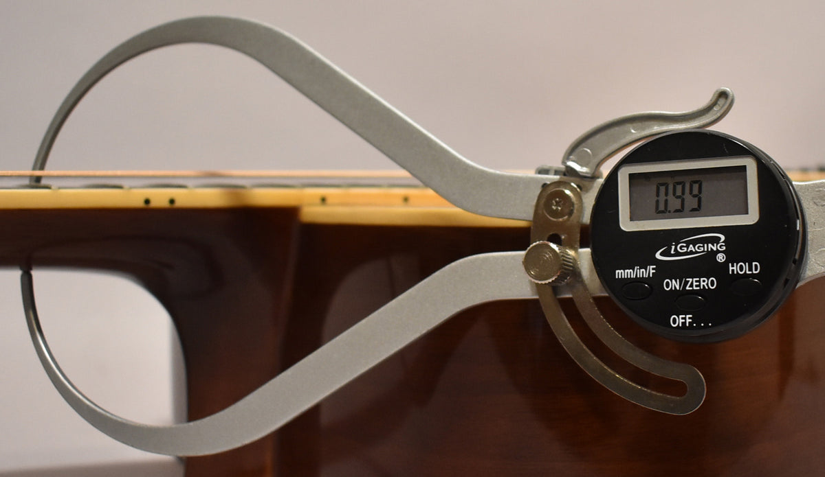A digital caliper measures the guitar's action at the 12th fret, showing 0.99mm between the low E string and the fretboard.