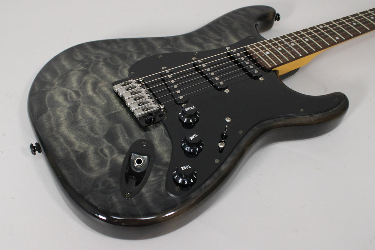 The electric guitar's translucent gray, flamed maple body with black pickguard, controls, and pickups is angled from the lower left.