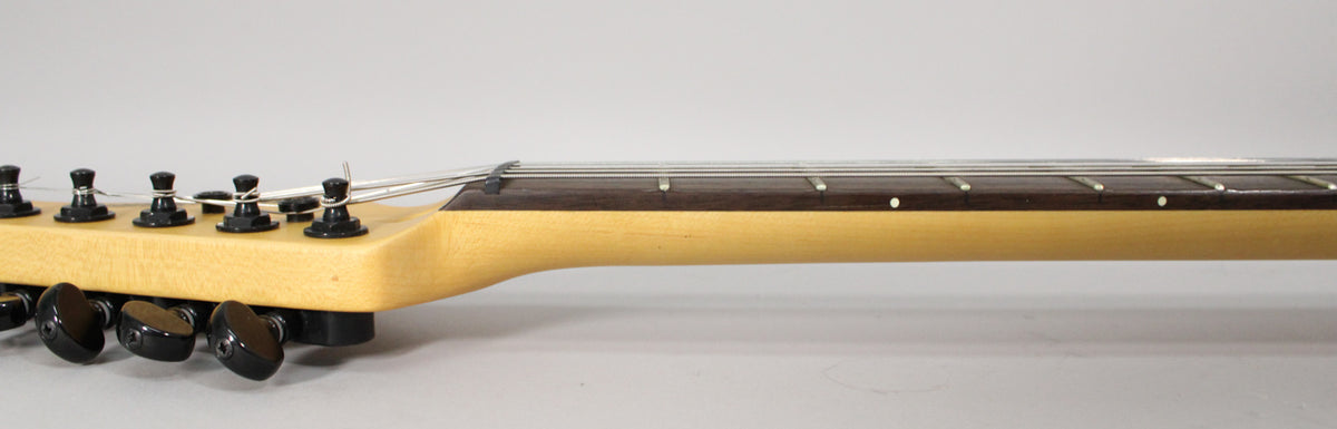 The guitar's light wood neck and dark fretboard are visible from the headstock to the 7th fret, with black tuners.