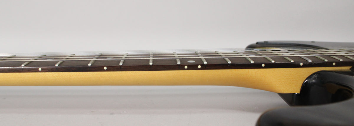 The guitar's neck and dark fretboard are visible from the side, with white dot inlays and silver frets.