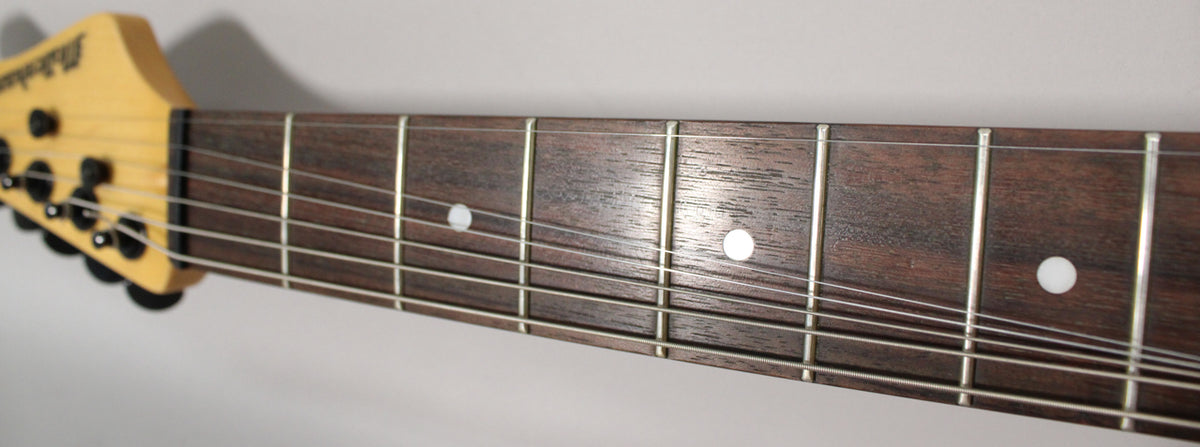 Close-up of the guitar's headstock and dark fretboard with white dot inlays, showing six strings and black tuning pegs.