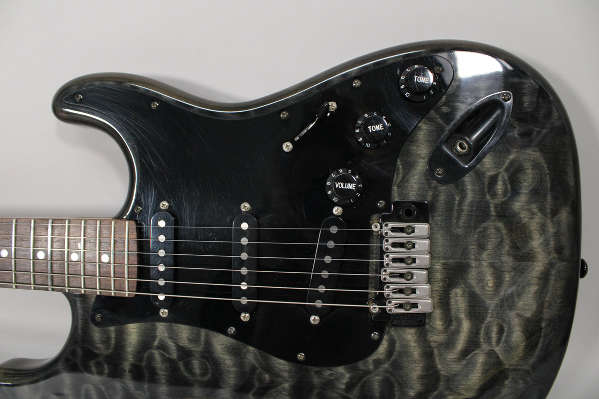 Upper body of a gray-black figured guitar with a black pickguard, three single-coil pickups, three black control knobs, and a chrome bridge.