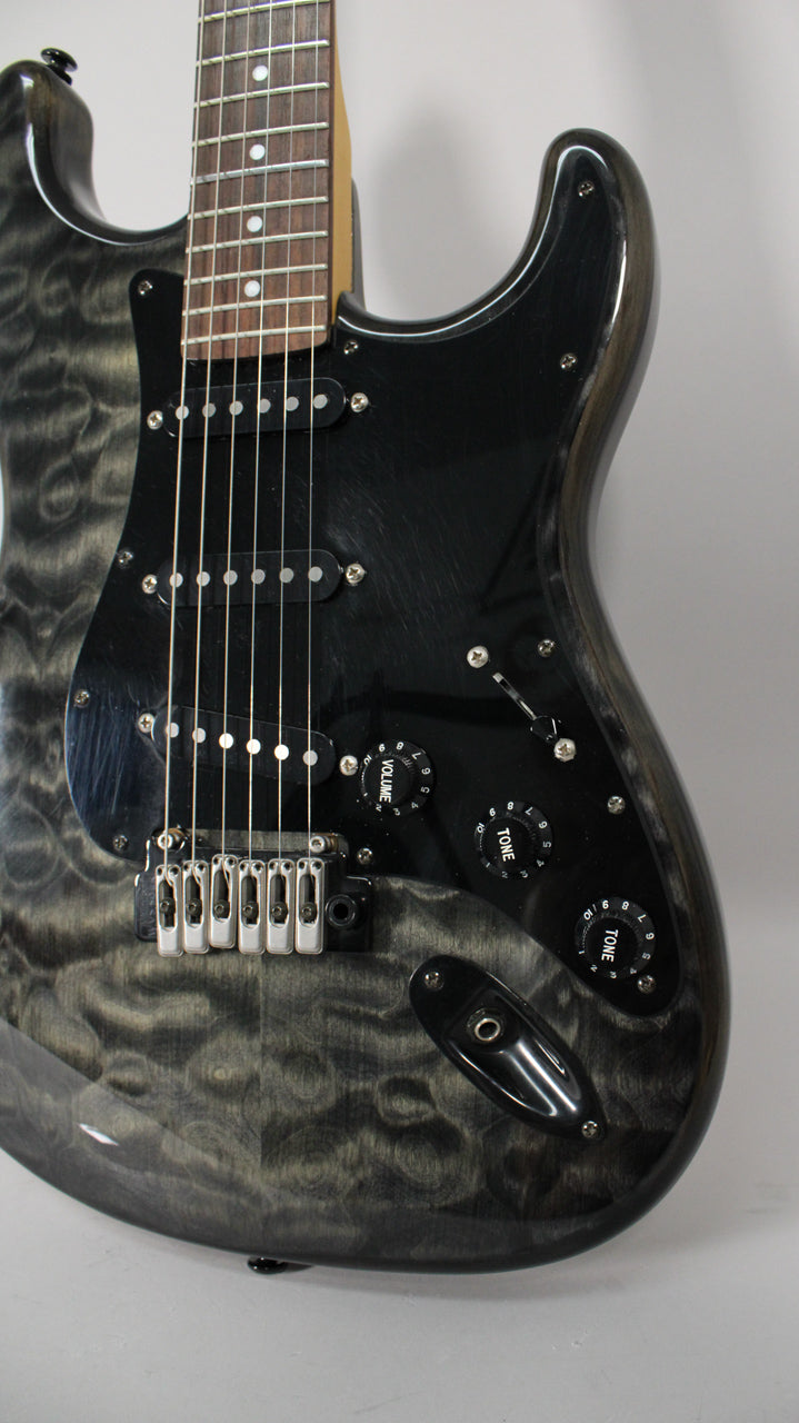 Close-up of a glossy trans gray electric guitar, showing the upper body, black pickguard, three single-coil pickups, and chrome bridge.