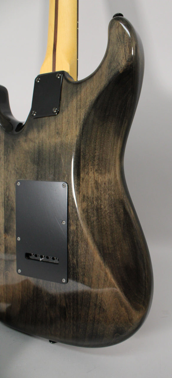 Rear view of a glossy trans gray electric guitar body with visible wood grain, black backplates, and a light-colored neck.