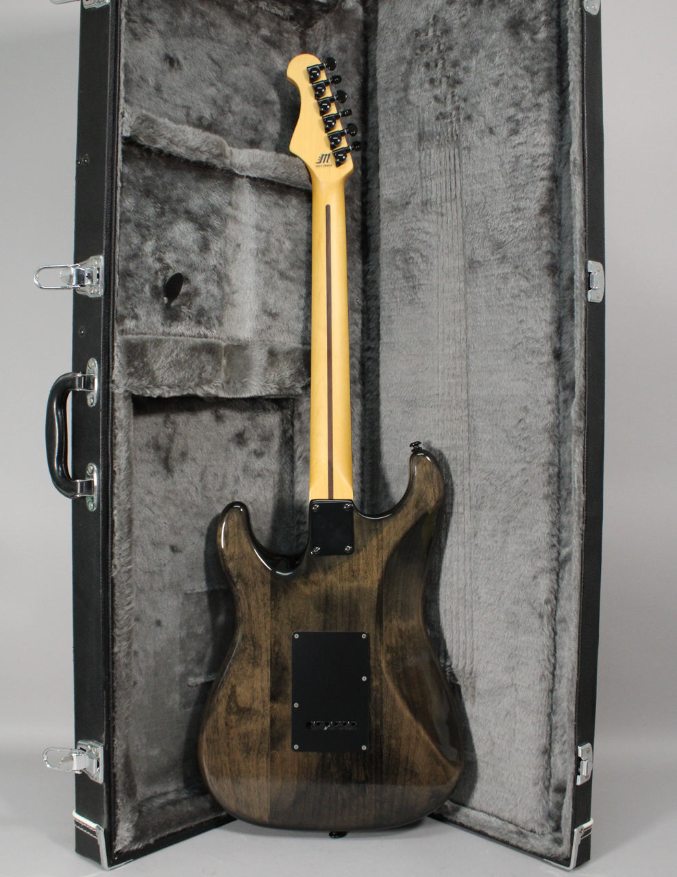 The back of a transparent gray electric guitar with a light maple neck, black hardware, and a black hard case.