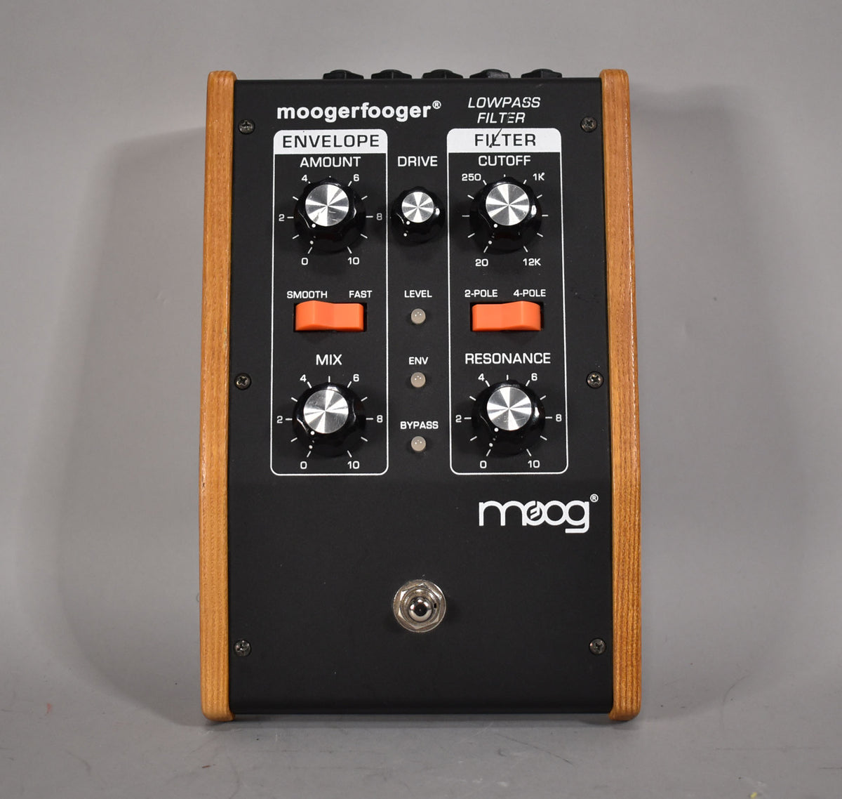 Top-down view of the black pedal with light wood sides, featuring six silver knobs, three orange toggle switches, and a footswitch.