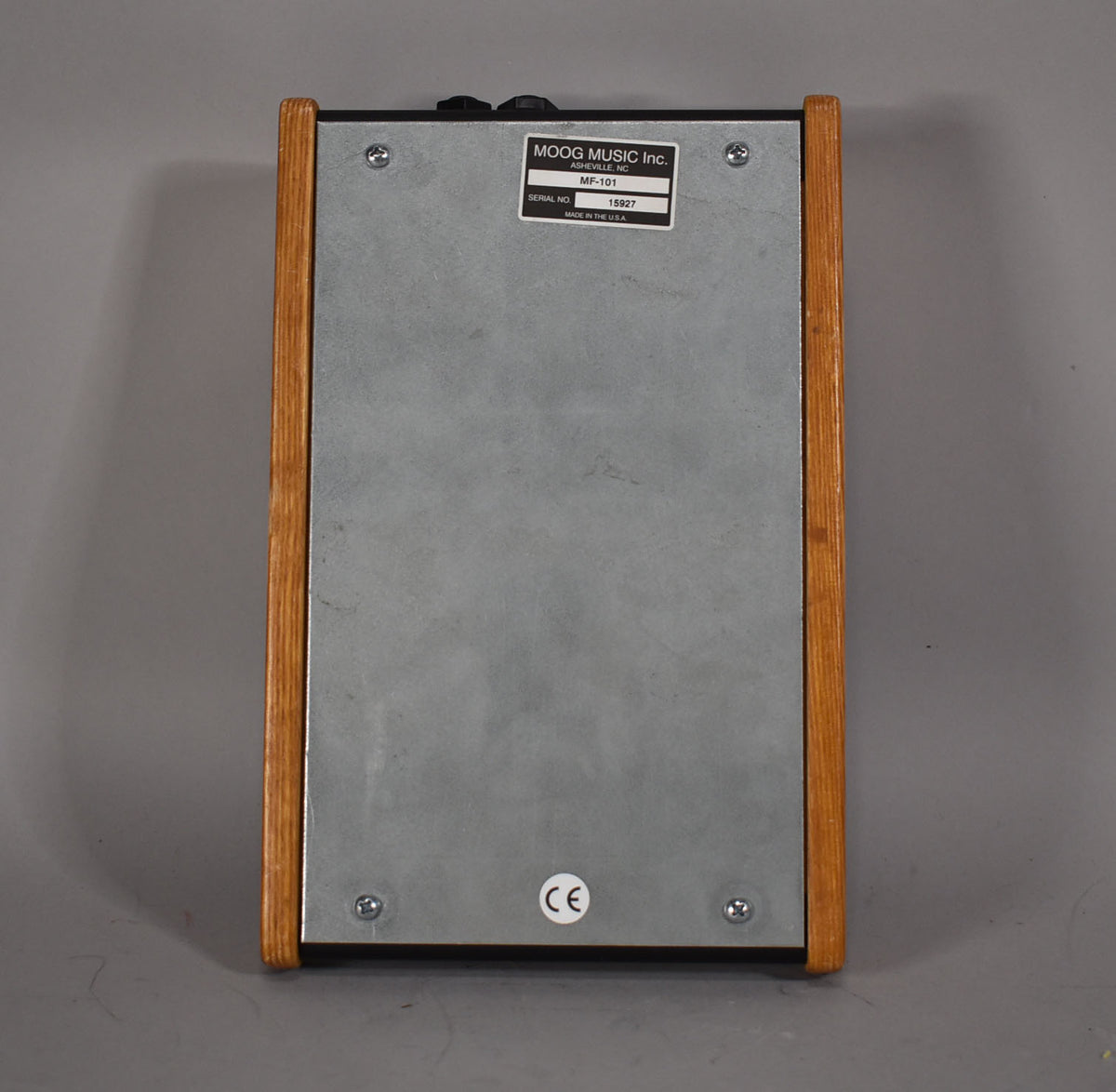 The pedal's metal bottom plate is visible, secured by four screws, with light wood side panels and a black label.