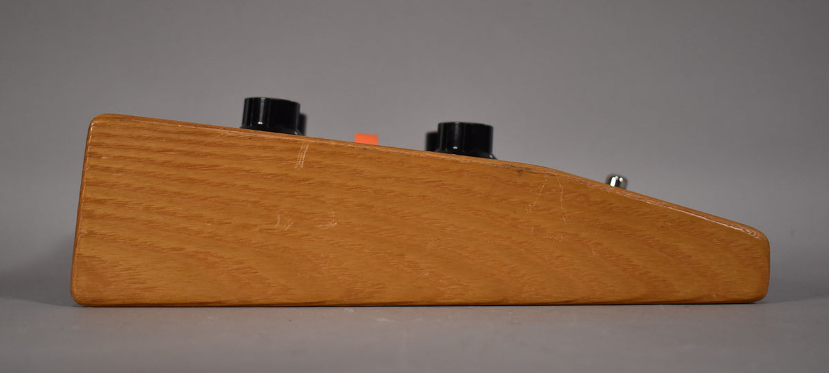 The effect pedal is shown from the right side, revealing its light brown wooden casing with visible grain and several surface scratches.