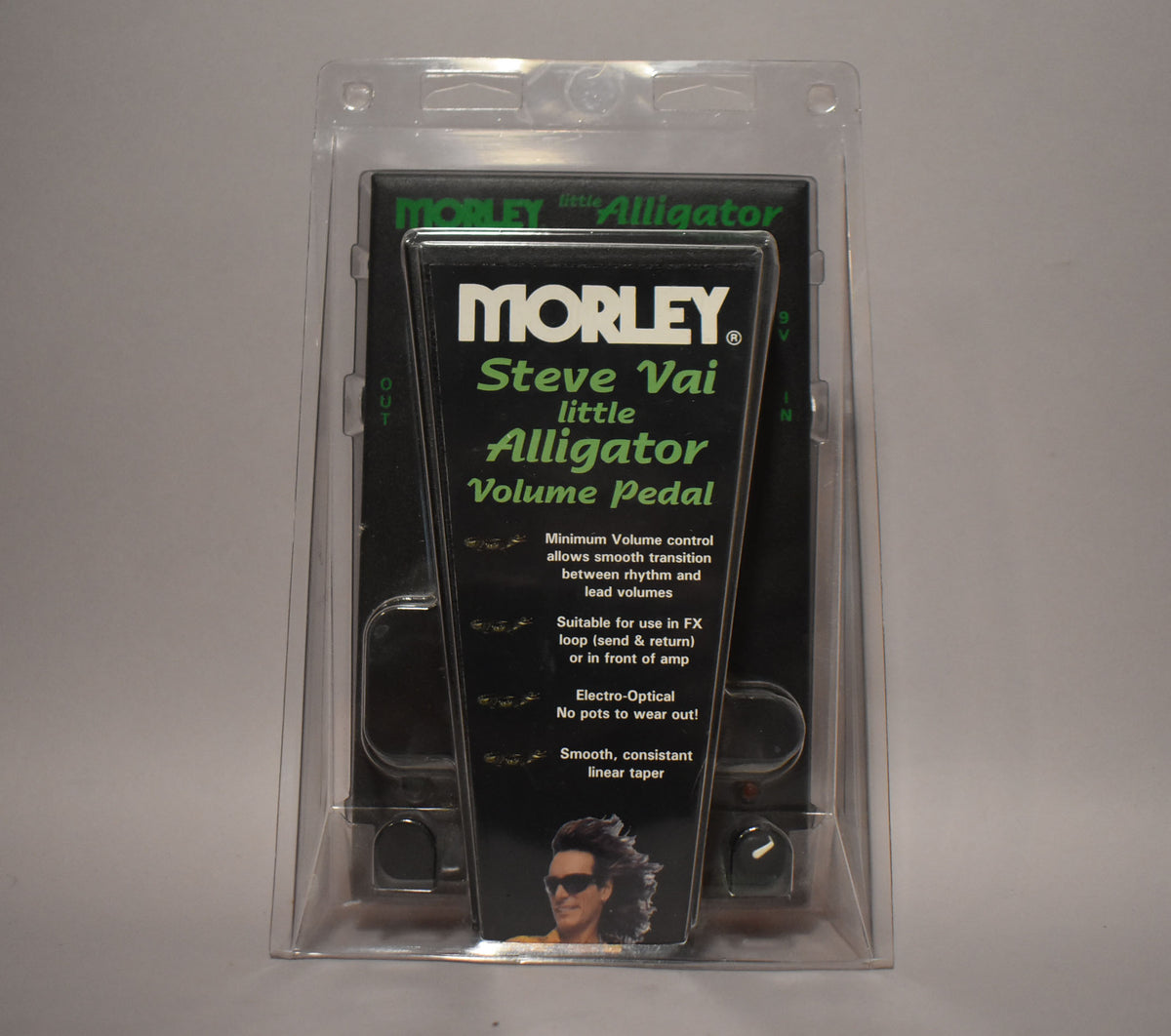 A clear plastic blister pack holds a black pedal with green lettering and a photo of Steve Vai, viewed from the front.