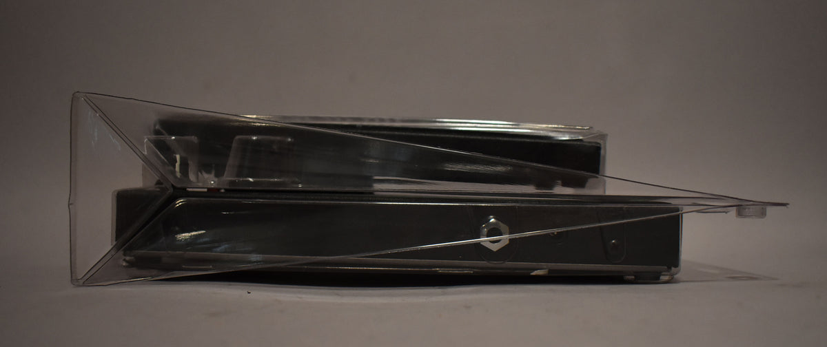 Side view of the black pedal in clear plastic packaging, showing a silver hexagonal input jack on the right.