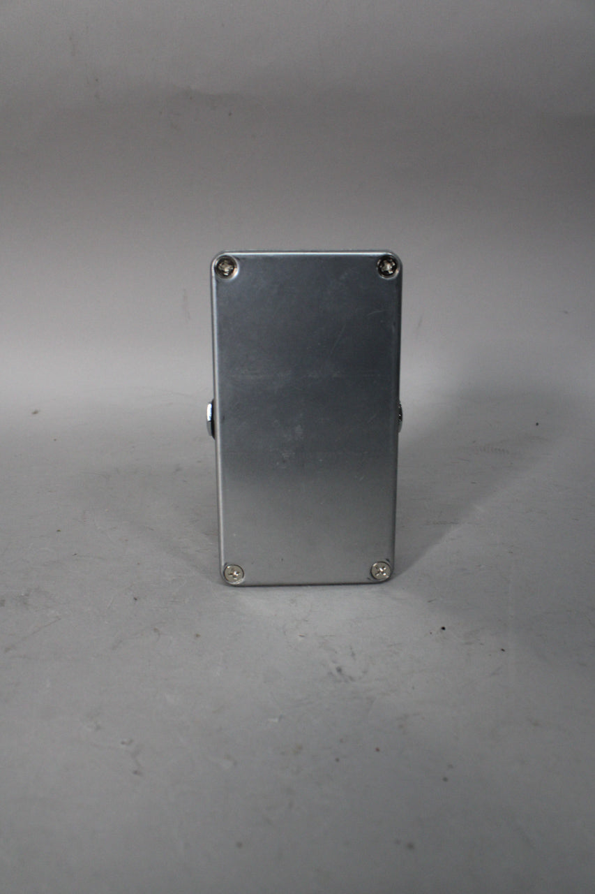 The back of a brushed silver rectangular guitar pedal is shown, secured by four visible screws and with minor scuffs.