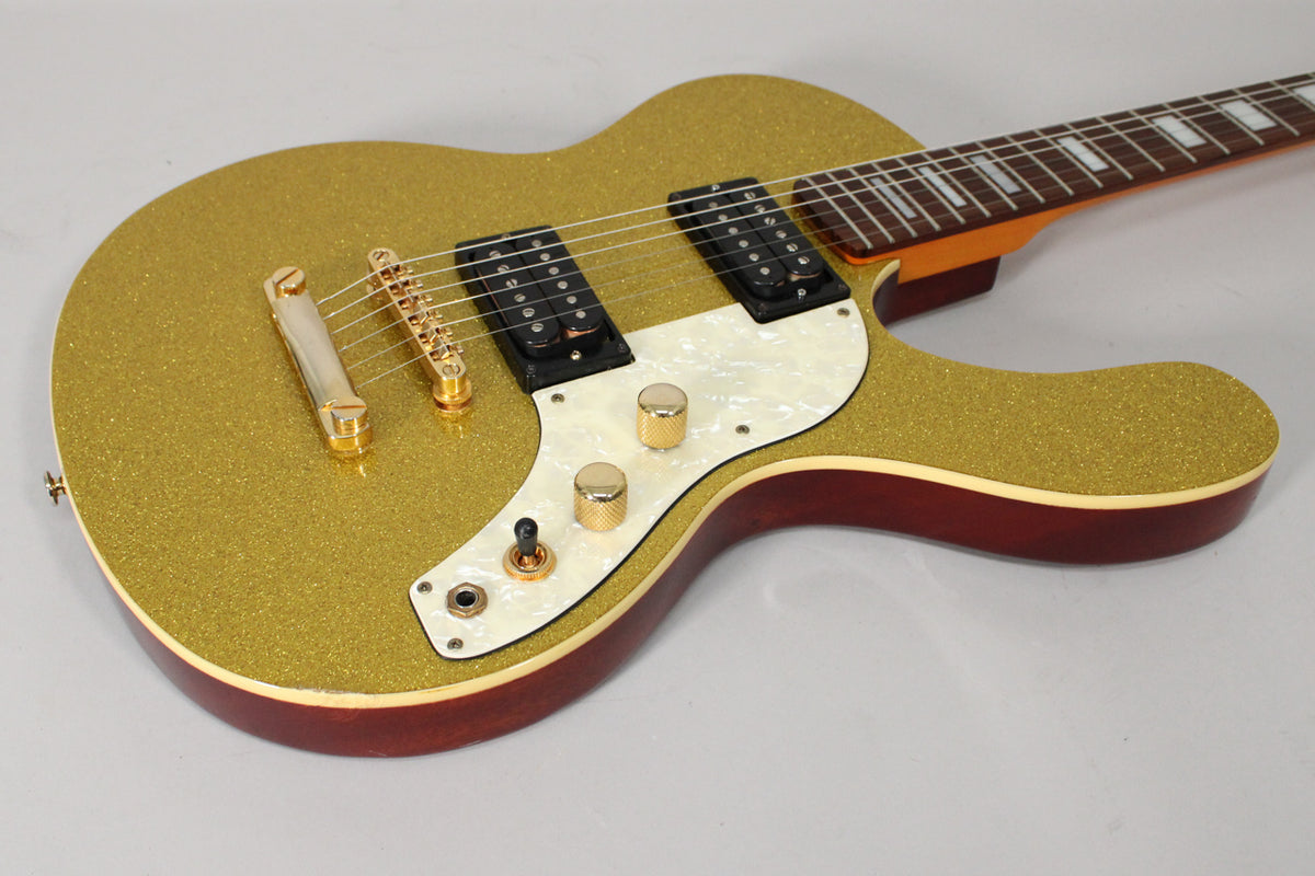 The gold sparkle guitar body, with two humbuckers, a pearloid pickguard, and gold hardware, is angled from the lower bout.